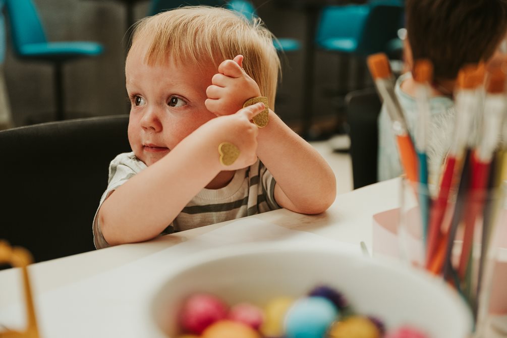 En liten gutt sitter ved et bord og har et klistremerke på hånden